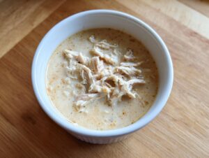 A white bowl filled with rich, creamy soup topped generously with shredded chicken, representing homemade cream of chicken soup.
