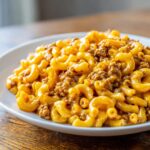 Close-up of creamy, cheesy homemade hamburger helper mixed with ground beef served on a white plate.