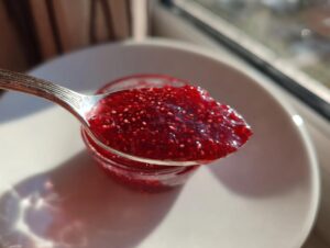 A spoonful of vibrant, thick raspberry jam, showing many seeds, held over a small jar.