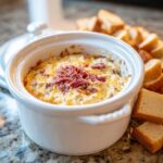 Close-up of a hot, baked Reuben dip topped with shredded corned beef, served alongside toasted bread slices.