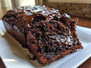 A close-up of a slice cut from a loaf of rich, dark hot fudge brownie bread topped with glossy chocolate glaze.