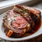 Close-up of perfectly cooked prime rib recipe slices showing a medium-rare center and herb crust, resting in au jus.