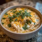 Close-up of a bowl of creamy keto white chicken chili topped with melted cheddar cheese and fresh cilantro.