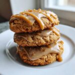 Three delicious maple cookies stacked on a white plate, topped with a thick maple icing and caramel drizzle.