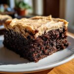 Close-up of a rich, dark chocolate banana bread brownies slice topped with thick peanut butter frosting.