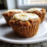 Close-up of moist carrot cake muffins topped with thick cream cheese frosting on a white plate.