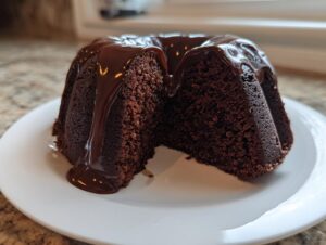 A slice removed from a small bundt-style moist chocolate cake, topped with glossy chocolate ganache.