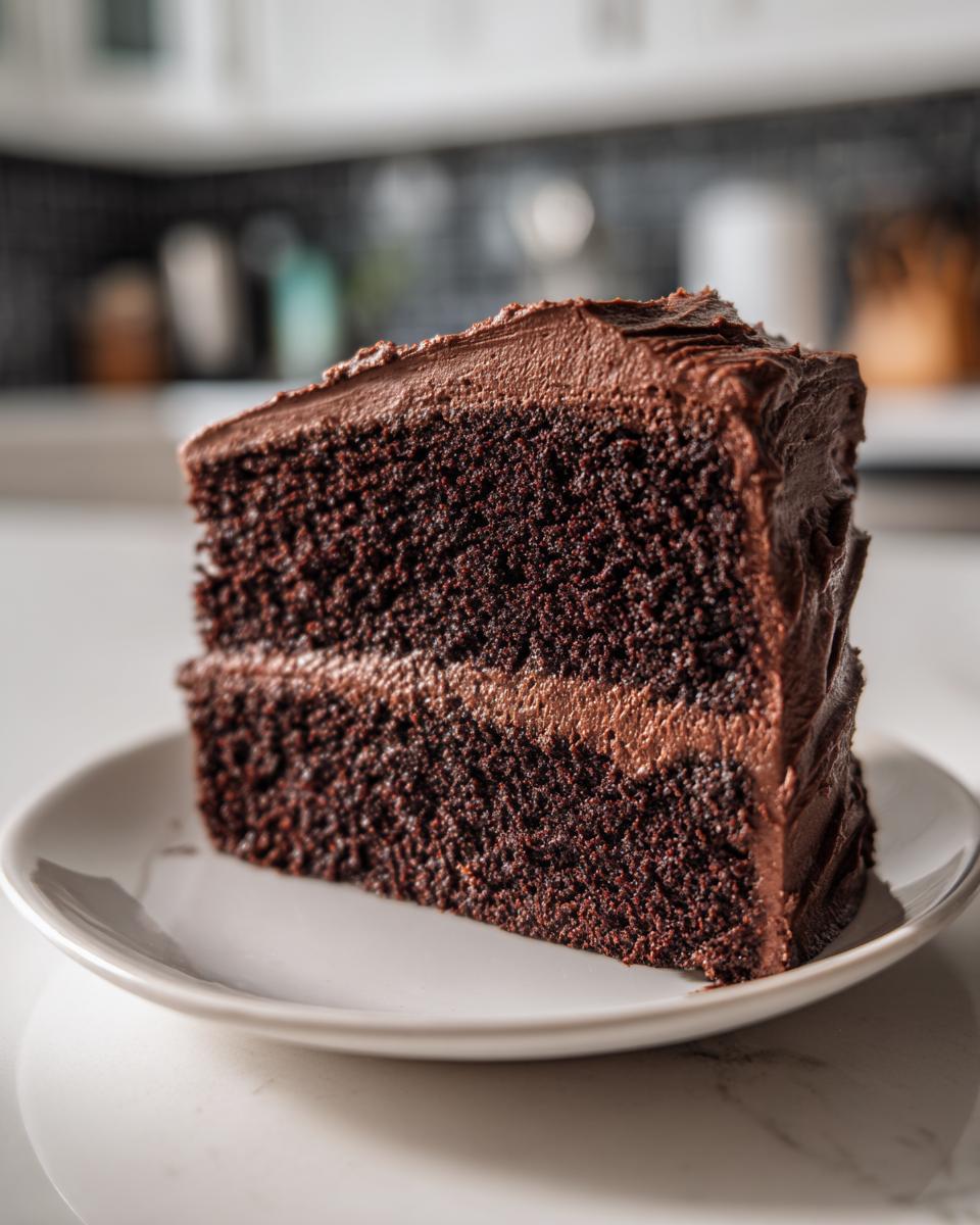 A close-up of a moist slice of two-layer chocolate cake covered in rich chocolate frosting.