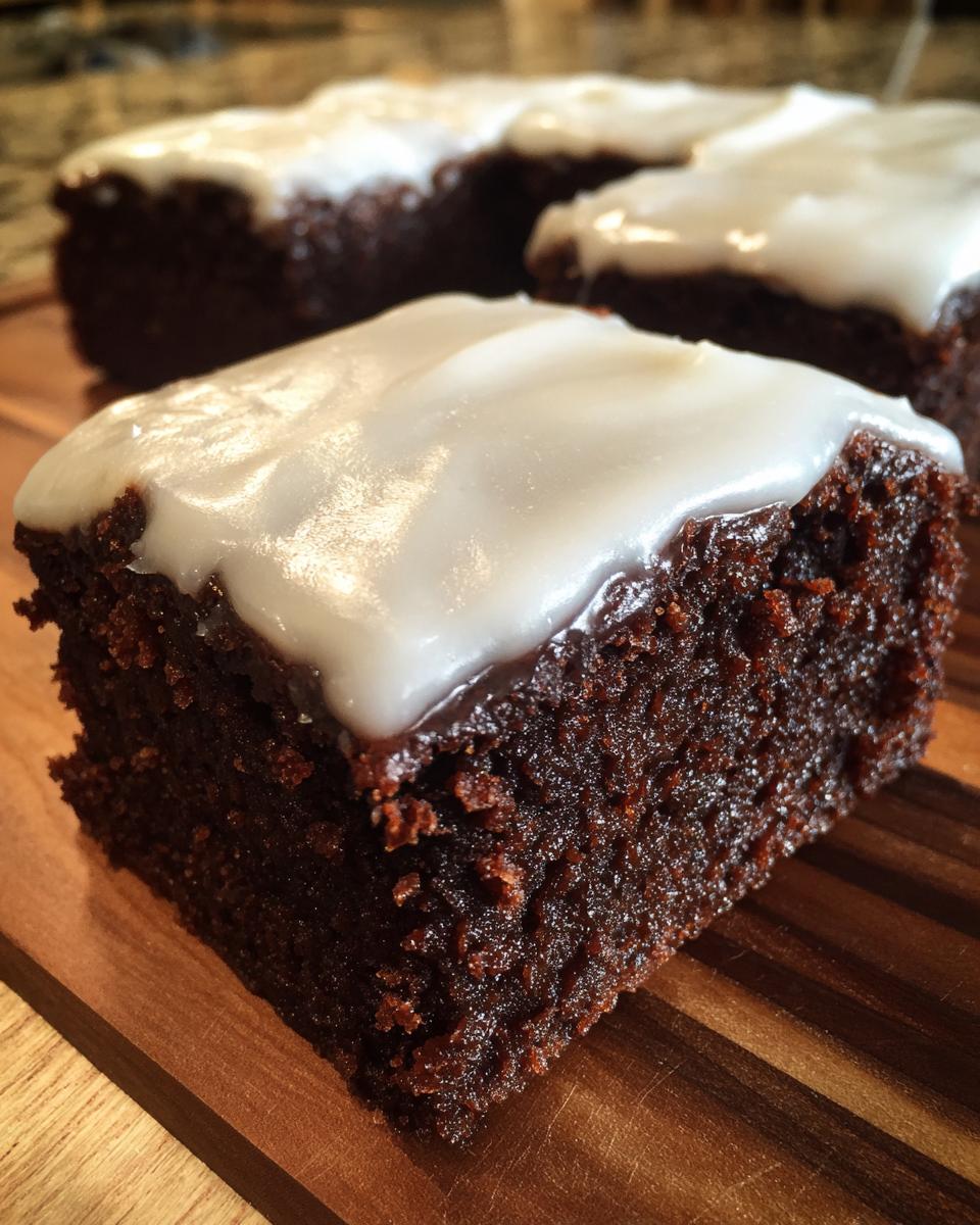 Close-up of a rich, dark square of gingerbread brownies topped with thick white icing, resting on a wooden board.