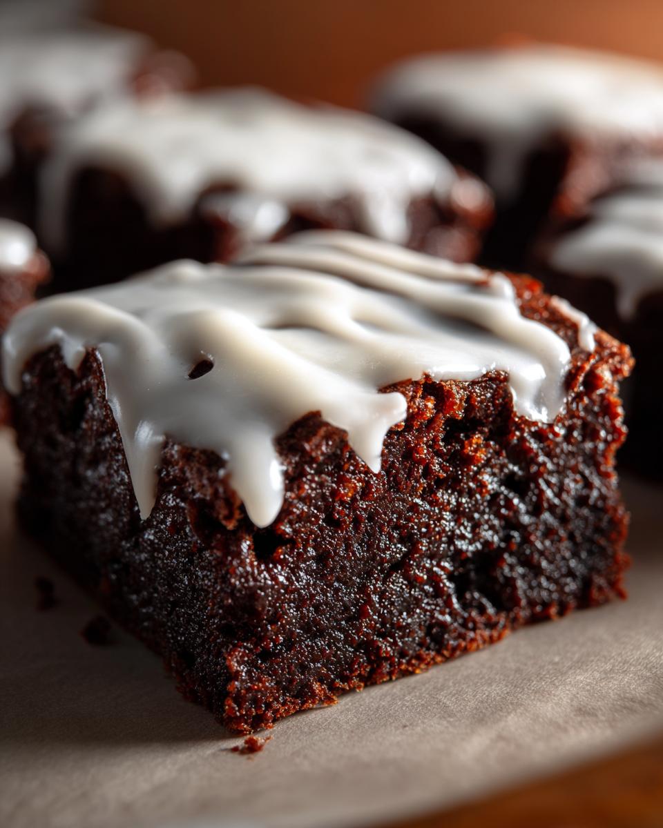 Close-up of a rich, dark gingerbread brownie square topped with thick white icing drizzle.