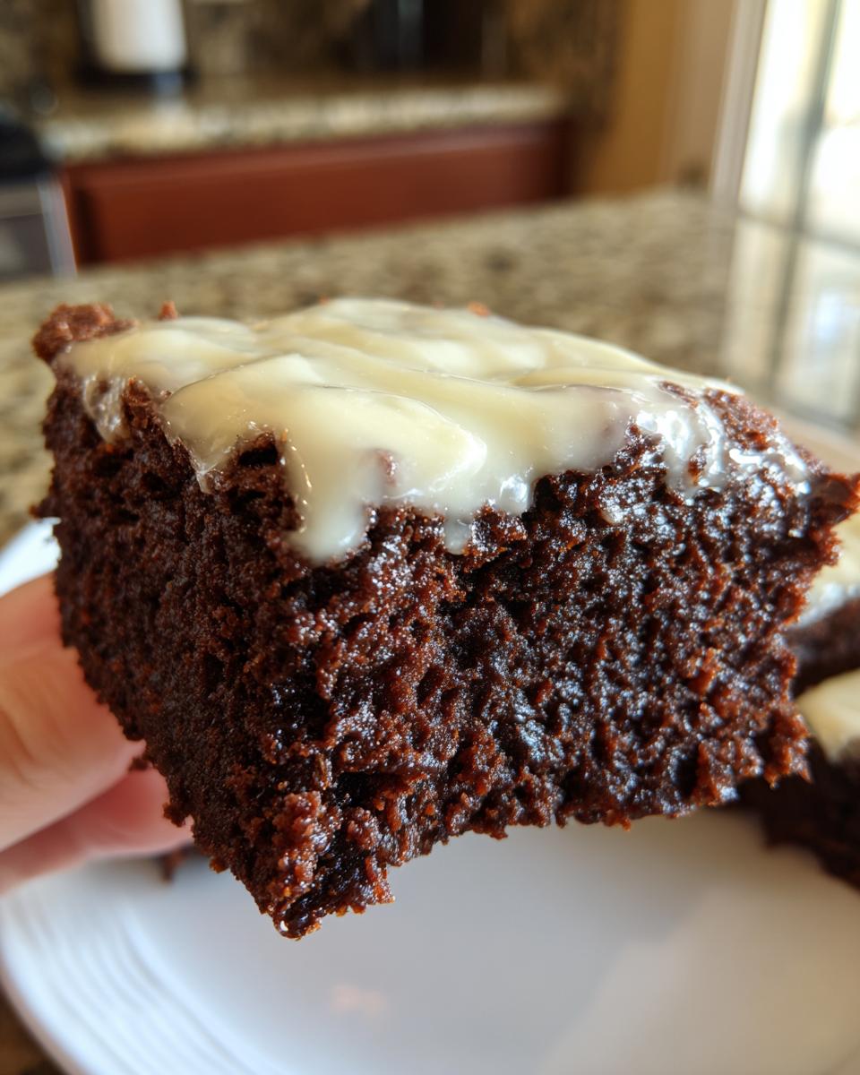 Close-up of a rich, dark slice of gingerbread brownies topped with thick white icing.