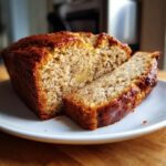 A close-up of a loaf of moist greek yogurt banana bread, sliced on a white plate.