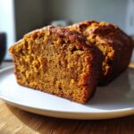 Close-up of a thick, moist slice of freshly baked pumpkin bread on a white plate.