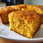 Close-up of a moist slice of sweet potato cornbread topped with a shiny orange glaze.