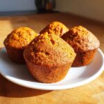 Four freshly baked, moist sweet potato muffins displayed prominently on a white plate.