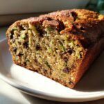 Close-up of a moist slice of zucchini banana bread showing green shreds of zucchini and dark chocolate chips throughout.