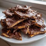 A close-up stack of broken pieces of peanut butter pretzel bark, featuring dark chocolate and a visible peanut butter layer.