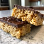 Two stacked peanut butter rice krispie treats bars, showing the crispy texture and thick chocolate topping.