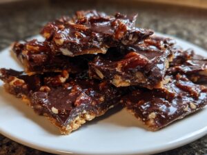 Close-up of several glistening, broken pieces of homemade pecan pie bark stacked on a white plate.