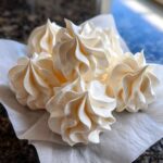 Close-up of several perfectly piped, creamy white meringue cookies resting on a white paper napkin.