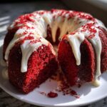 A vibrant red velvet bundt cake, sliced open, drizzled with white glaze and red sprinkles.