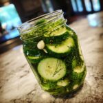 Close-up of sliced cucumbers, dill, and garlic in a jar making refrigerator pickles.