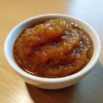A close-up of thick, rich brown pear butter served in a small white ramekin on a wooden surface.