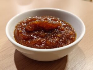 Close-up of thick, rich brown pear butter served in a small white bowl on a light wooden surface.