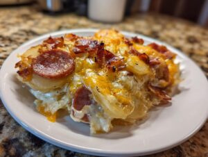 A close-up serving of cheesy pierogi casserole topped with melted cheddar and slices of browned sausage on a white plate.