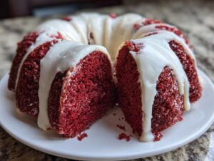 A close-up of a vibrant red velvet bundt cake sliced open, generously topped with dripping white cream cheese glaze.