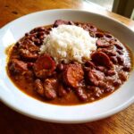 A white bowl filled with rich, saucy slow cooker red beans and rice topped with slices of smoked sausage.