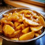 Close-up of thick, glistening apple pie filling slices coated in cinnamon sauce in a metal bowl.