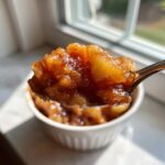 A spoonful of rich, cinnamon-spiced apple pie filling recipe held up against a bright window.