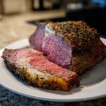 A juicy standing rib roast, perfectly cooked medium-rare, with one thick slice cut off, showing the herb crust.