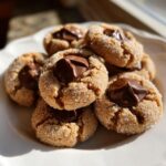 A pile of freshly baked peanut butter blossoms, rolled in sugar and topped with melted chocolate kisses.