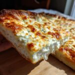 Close-up of a thick slice of white pizza showing a fluffy crust and generous layer of melted, browned cheese.