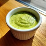 A small white ramekin filled with thick, vibrant green cilantro lime sauce, sitting on a wooden surface.