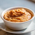 A close-up of freshly whipped cinnamon butter, rich brown in color, served in a small white ramekin.