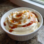 A close-up of creamy whipped ricotta dip swirled high in a white ramekin, topped with a drizzle of amber-colored caramel sauce.
