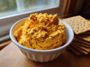 A bowl filled with bright orange pumpkin fluff dip served next to a stack of graham crackers.