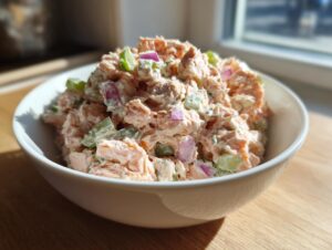 Close-up of creamy salmon salad mixed with celery and red onion, served in a white bowl.