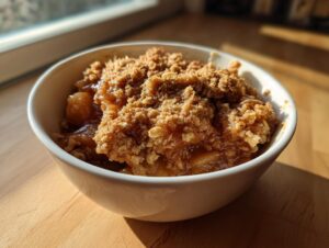 Close-up of a single serving of amazing apple crisp recipe in a white bowl, featuring bubbly fruit filling and a crunchy oat topping.