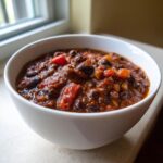 Close-up of a white bowl filled with rich, dark black bean chili, featuring visible chunks of tomato and beans.