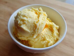 Two scoops of creamy, yellow cheese grits served in a small white bowl on a wooden surface.