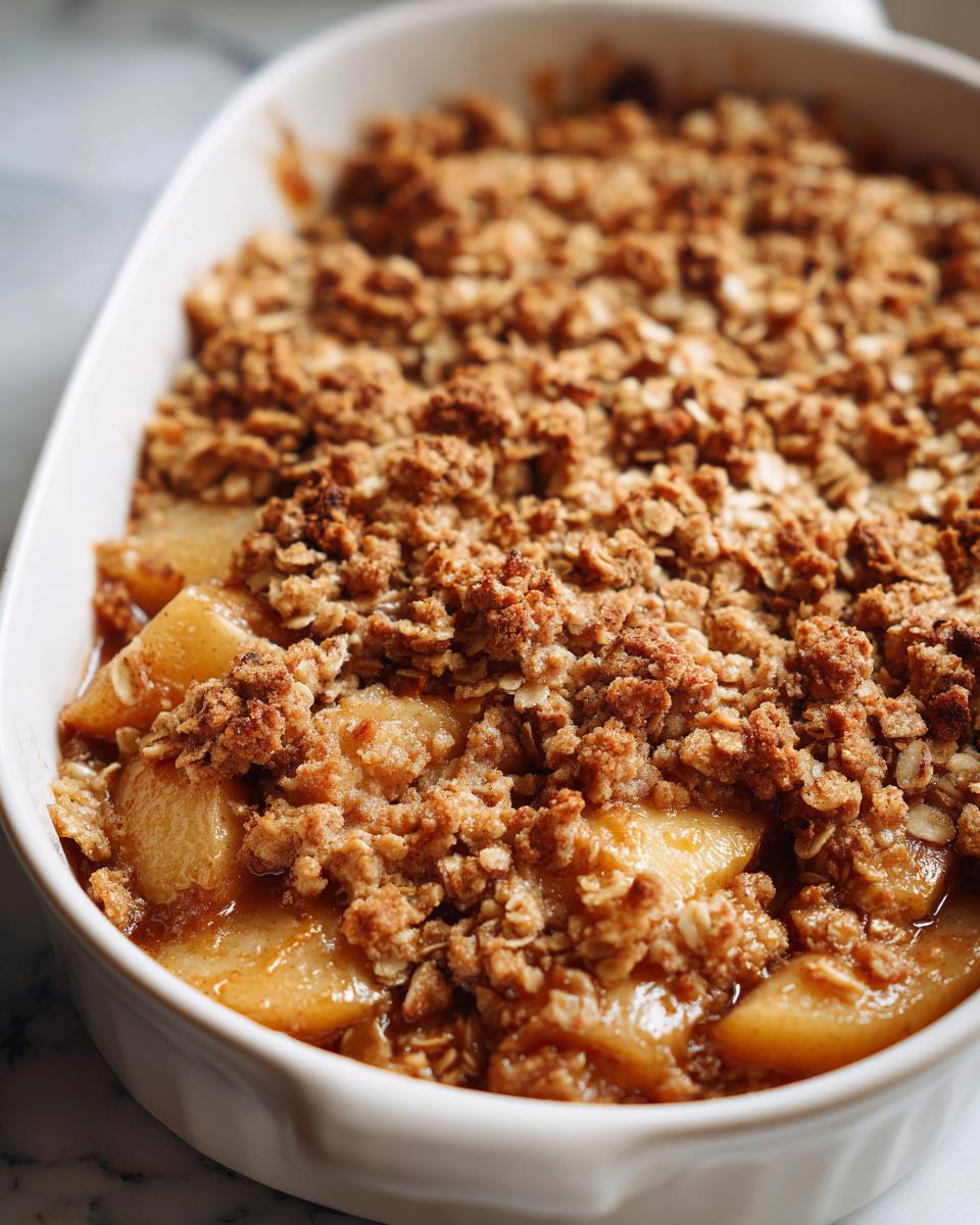 Close-up of a warm pear crisp in a white baking dish, showing soft baked pears under a crunchy, buttery oat topping.