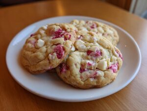 Three chewy white chocolate raspberry cookies stacked slightly on a white plate.