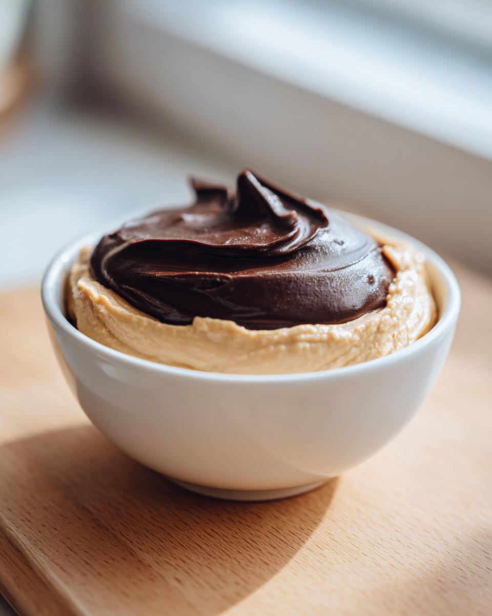 A white bowl filled with creamy peanut butter dip topped with a swirl of rich, dark chocolate ganache.