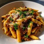 A close-up of a bowl of creamy beef pasta made with penne, topped with grated cheese and fresh parsley.