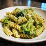 Close-up of creamy broccoli pasta featuring fusilli noodles and bright green broccoli florets, topped with grated cheese.