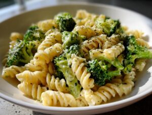 Close-up of creamy broccoli pasta featuring fusilli noodles and bright green broccoli florets, topped with herbs and cheese.